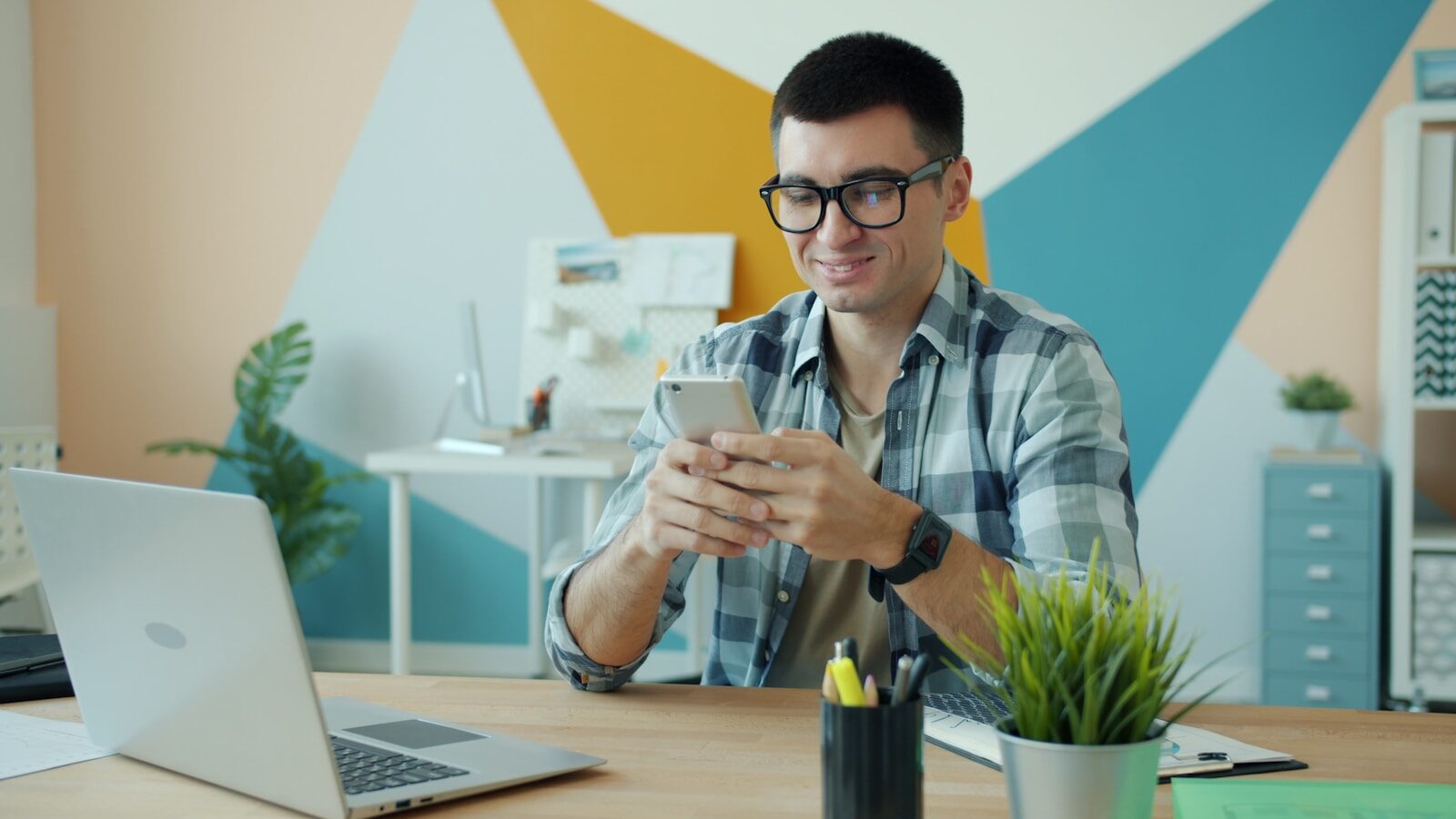 Man in glasses using phone at office desk.